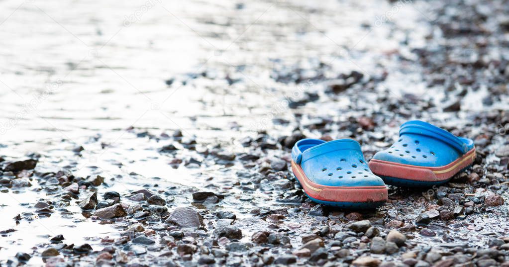 Pair of blue flip flops on the beach filled with tiny stones and pebbles.