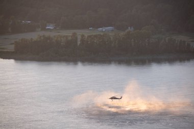 Kadar yakın çekim helikopterin eğitim kurtarma operasyonu Columbia Nehri üzerinde günbatımında. Su sıçramalarına, buharı ve spreyler nehir yüzeyden ayağa kalkın. Helikopterden ip asılı.