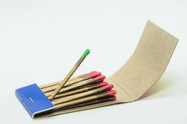 Isolated paper matchbox with all matches having red head while one sticking out match has a green one. Conceptual image for being different from others.