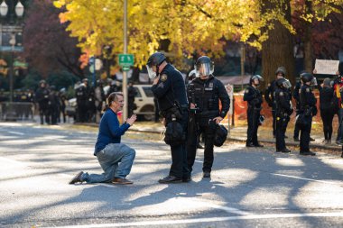 Portland, ya da / Amerika Birleşik Devletleri - 17 Kasım 2018: gösterici şehir Portland bir sokak ortasında dizlerinin üzerinde. İki polis memuru ile yetişkin bir erkek ikna etmeye çalışır.