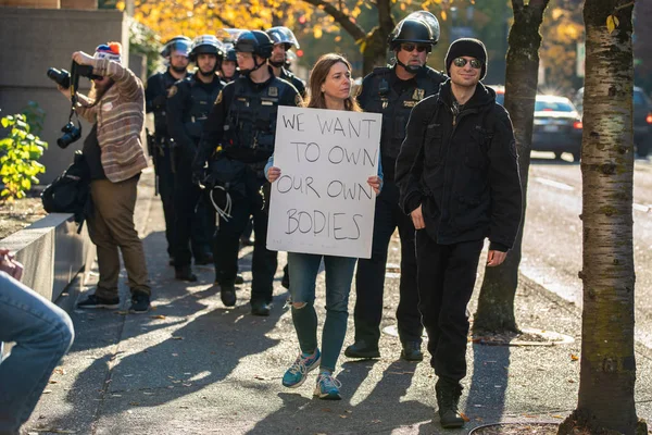 ポートランド または アメリカ合衆国 2018 ダウンタウンのデモで彼女の後ろに暴動鎮圧用装備の警察で 私たちは私たち自身体を所有したい という記号を保持している女性 — ストック写真
