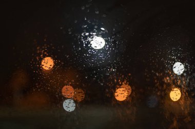 Yağmur damlaları parlıyor sokak ışıkları ile gece arabanın ön cam üzerinde.