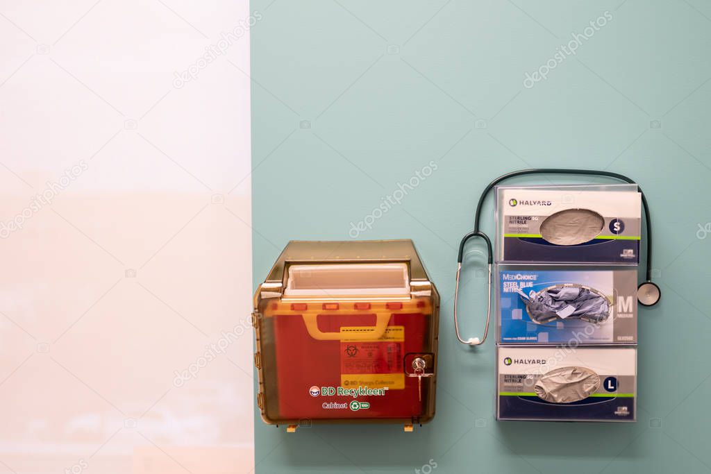 Portland, OR / USA - December 14 2018: Doctor office wall with medical box for storage and disposal of used needles, glove boxes and phonendoscope.