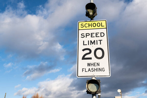 Speed limit 20 when flashing sign near school. Cloudy sky in the background.