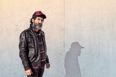 40 'larında, kırmızı şapkalı, oduncu gömlekli ve beton duvarın önünde siyah deri ceketli sakallı bir Latin adamın portresi..