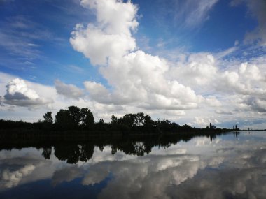 Mavi gökyüzü ve bulutlar sakin nehirde yansıtan Gölü