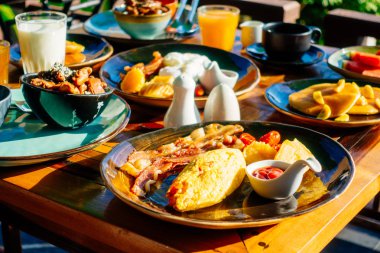 Sağlıklı kahvaltı seti yumurta pastırma ile portakal suyu süt ekmek kahve ve diğer ahşap masada krep