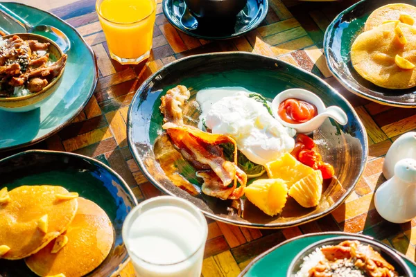 Sağlıklı kahvaltı seti yumurta pastırma ile portakal suyu süt ekmek kahve ve diğer ahşap masada krep