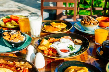Sağlıklı kahvaltı seti yumurta pastırma ile portakal suyu süt ekmek kahve ve diğer ahşap masada krep