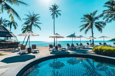 Güzel tropikal plaj ve deniz şemsiyesi ve sandalyesi otel tatil ve tatil için yüzme havuzunda.