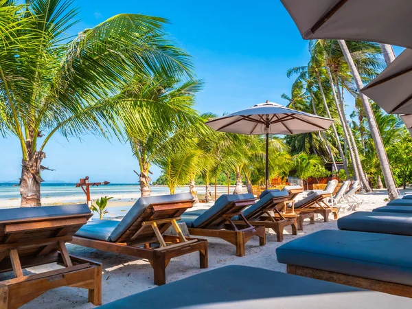 Şemsiye ve sandalyenin üstüne Hindistan cevizi hurma ağacının seyahat ve tatil etrafında mavi gökyüzü ile plaj ve okyanus