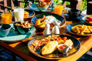 Sağlıklı kahvaltı seti yumurta pastırma ile portakal suyu süt ekmek kahve ve diğer ahşap masada krep