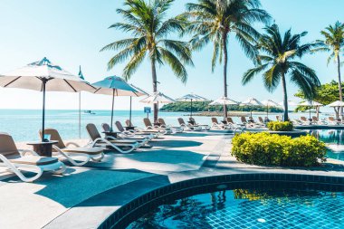 Güzel tropikal plaj ve deniz şemsiyesi ve sandalyesi otel tatil ve tatil için yüzme havuzunda.