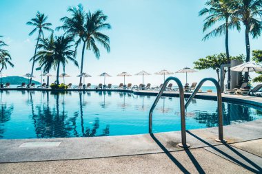 Güzel tropikal plaj ve deniz şemsiyesi ve sandalyesi otel tatil ve tatil için yüzme havuzunda.