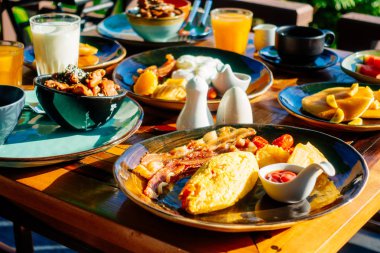 Sağlıklı kahvaltı seti yumurta pastırma ile portakal suyu süt ekmek kahve ve diğer ahşap masada krep