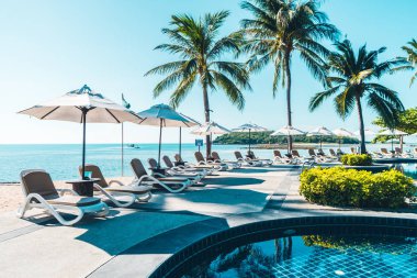 Güzel tropikal plaj ve deniz şemsiyesi ve sandalyesi otel tatil ve tatil için yüzme havuzunda.