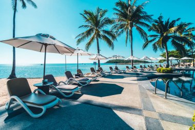 Güzel tropikal plaj ve deniz şemsiyesi ve sandalyesi otel tatil ve tatil için yüzme havuzunda.