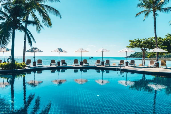 Güzel tropikal plaj ve deniz şemsiyesi ve sandalyesi otel tatil ve tatil için yüzme havuzunda.