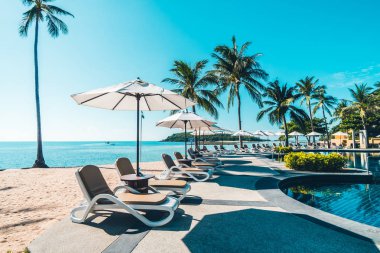 Güzel tropikal plaj ve deniz şemsiyesi ve sandalyesi otel tatil ve tatil için yüzme havuzunda.