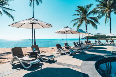 Güzel tropikal plaj ve deniz şemsiyesi ve sandalyesi otel tatil ve tatil için yüzme havuzunda.