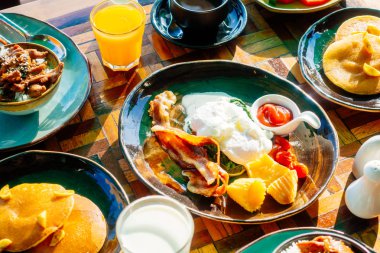 Sağlıklı kahvaltı seti yumurta pastırma ile portakal suyu süt ekmek kahve ve diğer ahşap masada krep