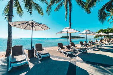 Güzel tropikal plaj ve deniz şemsiyesi ve sandalyesi otel tatil ve tatil için yüzme havuzunda.