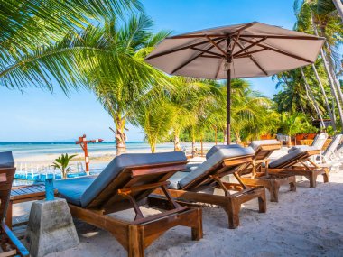 Şemsiye ve sandalyenin üstüne Hindistan cevizi hurma ağacının seyahat ve tatil etrafında mavi gökyüzü ile plaj ve okyanus