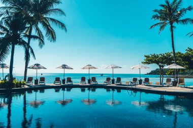 Güzel tropikal plaj ve deniz şemsiyesi ve sandalyesi otel tatil ve tatil için yüzme havuzunda.