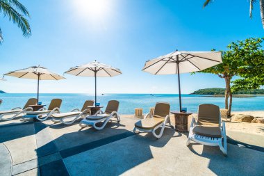 Güzel tropikal plaj ve deniz şemsiyesi ve sandalyesi otel tatil ve tatil için yüzme havuzunda.