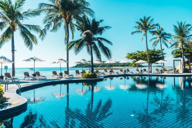 Güzel tropikal plaj ve deniz şemsiyesi ve sandalyesi otel tatil ve tatil için yüzme havuzunda.