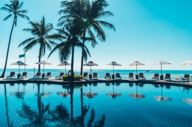 Güzel tropikal plaj ve deniz şemsiyesi ve sandalyesi otel tatil ve tatil için yüzme havuzunda.