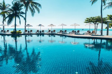 Güzel tropikal plaj ve deniz şemsiyesi ve sandalyesi otel tatil ve tatil için yüzme havuzunda.