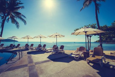 Güzel tropikal plaj ve deniz şemsiyesi ve sandalyesi otel tatil ve tatil için yüzme havuzunda.