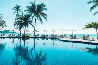 Güzel tropikal plaj ve deniz şemsiyesi ve sandalyesi otel tatil ve tatil için yüzme havuzunda.