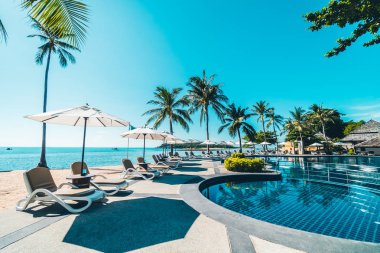 Güzel tropikal plaj ve deniz şemsiyesi ve sandalyesi otel tatil ve tatil için yüzme havuzunda.