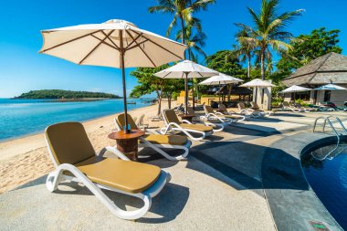 Güzel tropikal plaj ve deniz şemsiyesi ve sandalyesi otel tatil ve tatil için yüzme havuzunda.