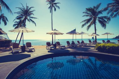 Güzel tropikal plaj ve deniz şemsiyesi ve sandalyesi otel tatil ve tatil için yüzme havuzunda.