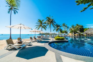 Güzel tropikal plaj ve deniz şemsiyesi ve sandalyesi otel tatil ve tatil için yüzme havuzunda.