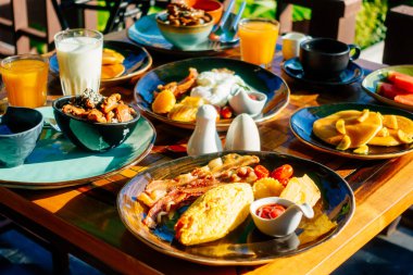 Sağlıklı kahvaltı seti yumurta pastırma ile portakal suyu süt ekmek kahve ve diğer ahşap masada krep