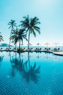 Güzel tropikal plaj ve deniz şemsiyesi ve sandalyesi otel tatil ve tatil için yüzme havuzunda.