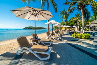 Güzel tropikal plaj ve deniz şemsiyesi ve sandalyesi otel tatil ve tatil için yüzme havuzunda.