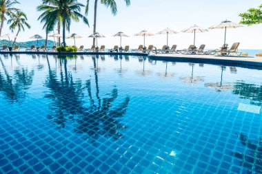 Güzel tropikal plaj ve deniz şemsiyesi ve sandalyesi otel tatil ve tatil için yüzme havuzunda.