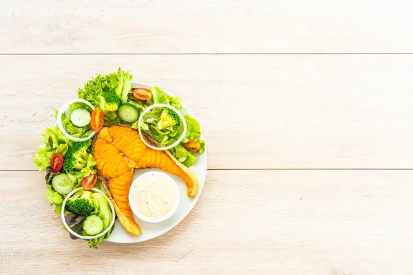 烤三文鱼牛排与新鲜蔬菜和酱汁在木桌上 健康食物概念 — 图库照片