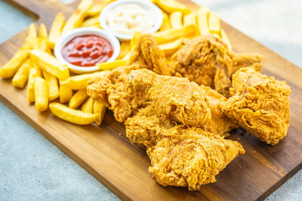 Fried chicken wings with french fries and tomato or ketchup and mayonnaise sauce on wood cutting board - Junk or Unhealthy food style