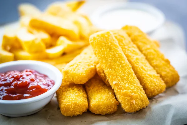 stock image Fish finger and french fries or chips with tomato ketchup and mayonnaise sauce on wooden cutting board - Unhealthy food style