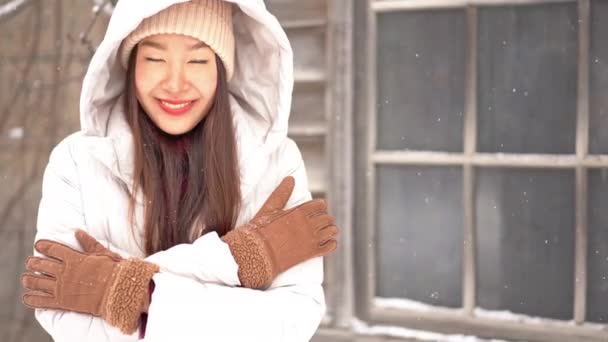 美丽的亚洲女人在冬季夹克在雪下看着相机的镜头 — 图库视频影像