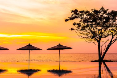 Şemsiye ve eğlence seyahat ve tatil için gündoğumu veya günbatımı saatinde deniz okyanusu plaja yakın yüzme havuzu etrafında sandalye