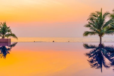 Tatil ve seyahat için gün doğumu veya günbatımı saatinde otel ve tatil beldesinde yüzme havuzu etrafında hindistan cevizi palmiye ağacı ile açık güzel manzara