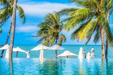 Şemsiye ve sandalye ve hindistan cevizi palmiye ağacı ile otel beldesinde güzel lüks açık yüzme havuzu