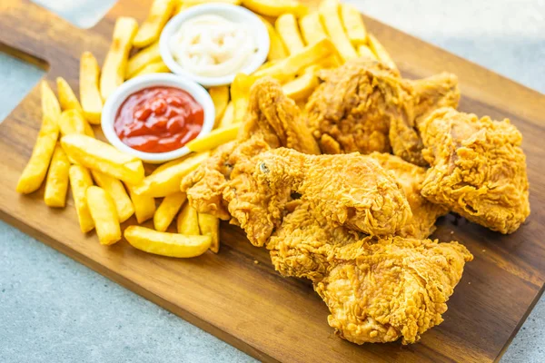 Fried chicken wings with french fries and tomato or ketchup and mayonnaise sauce on wood cutting board - Junk or Unhealthy food style